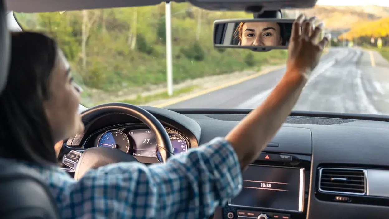 Mulher ao volante ajusta o espelho retrovisor interior num carro em estrada.