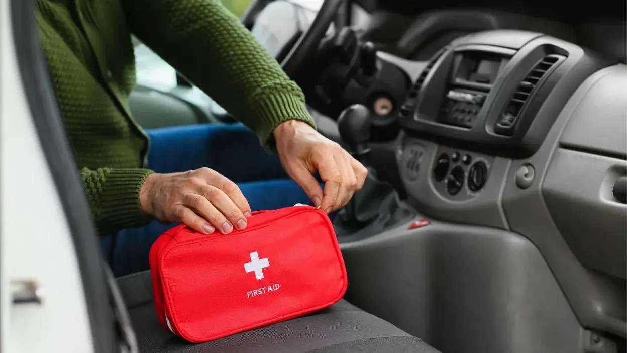 Pessoa a guardar um kit de primeiros socorros vermelho no banco do carro