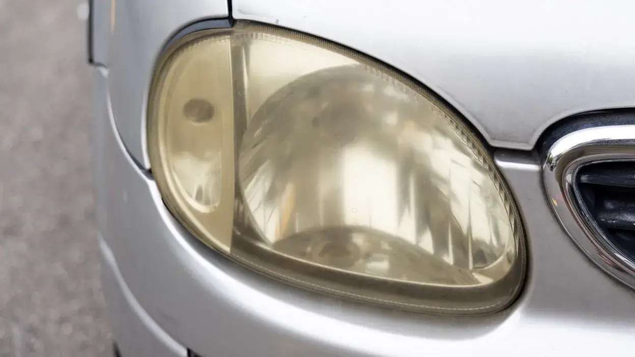 Farol dianteiro de carro com plástico amarelecido e opaco.