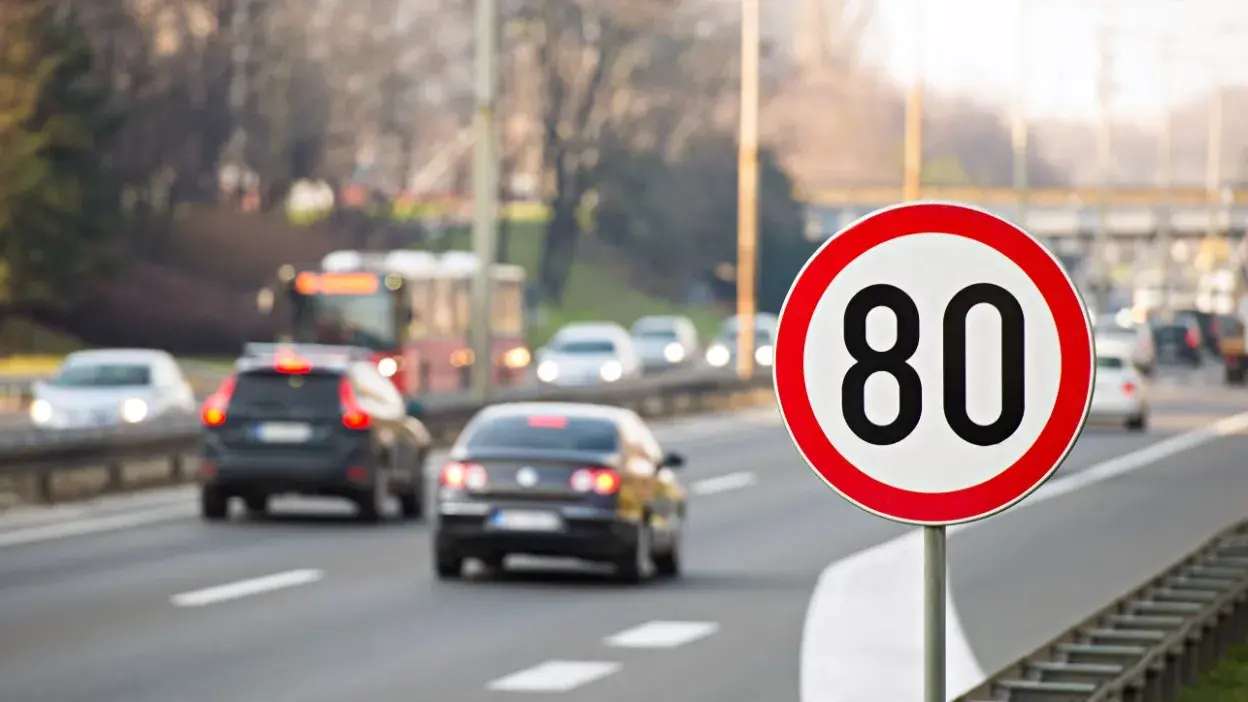 Sinal de trânsito com limite de velocidade de 80 km/h numa estrada com vários carros em movimento.