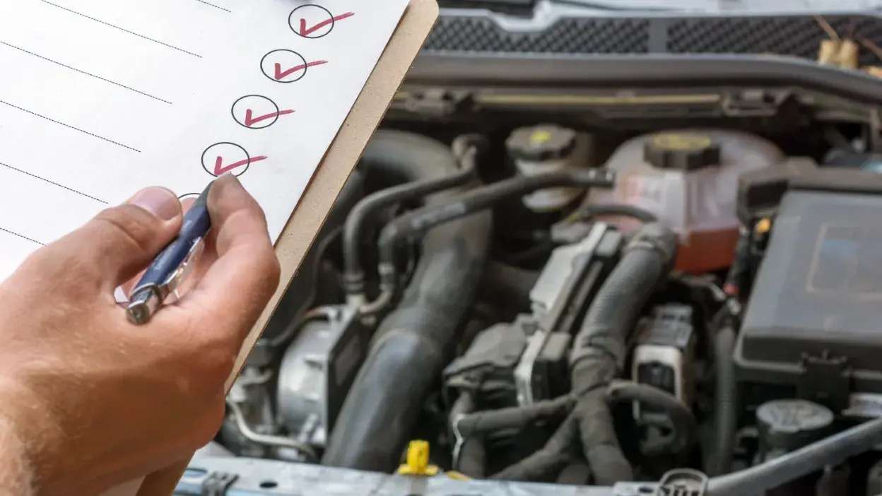 Pessoa a assinalar checklist durante inspeção ao motor do carro aberto