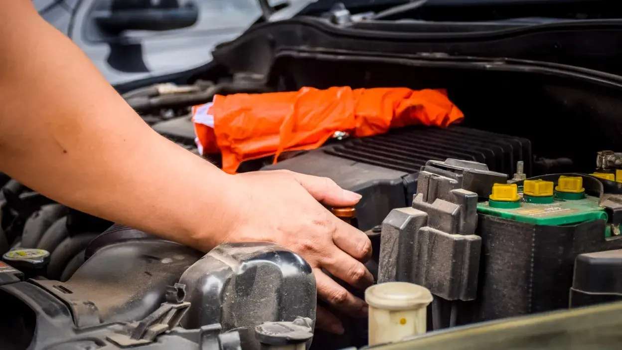 Mão a verificar o motor de um carro com um saco laranja no fundo do compartimento do motor.