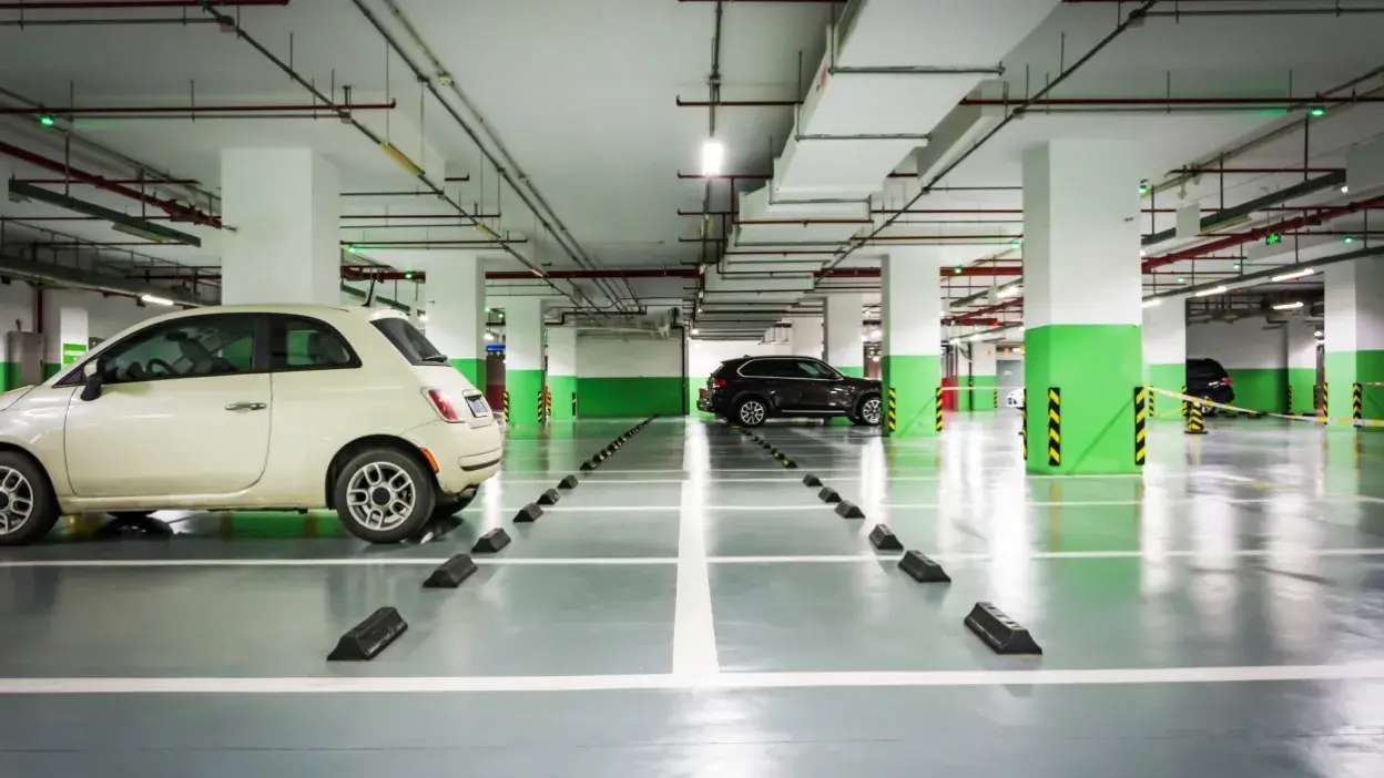 Parque de estacionamento interior com poucos carros estacionados e várias vagas livres delimitadas por linhas brancas e calços pretos.