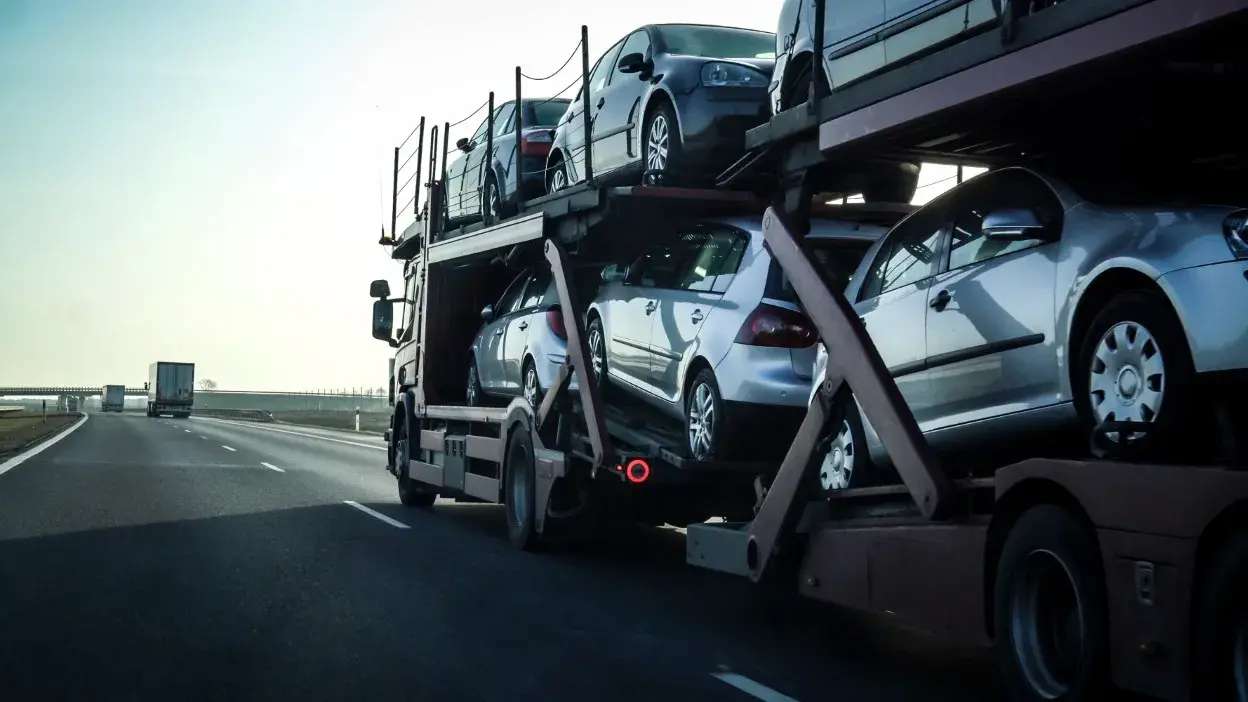Camioneta a transportar vários carros prateados numa autoestrada.