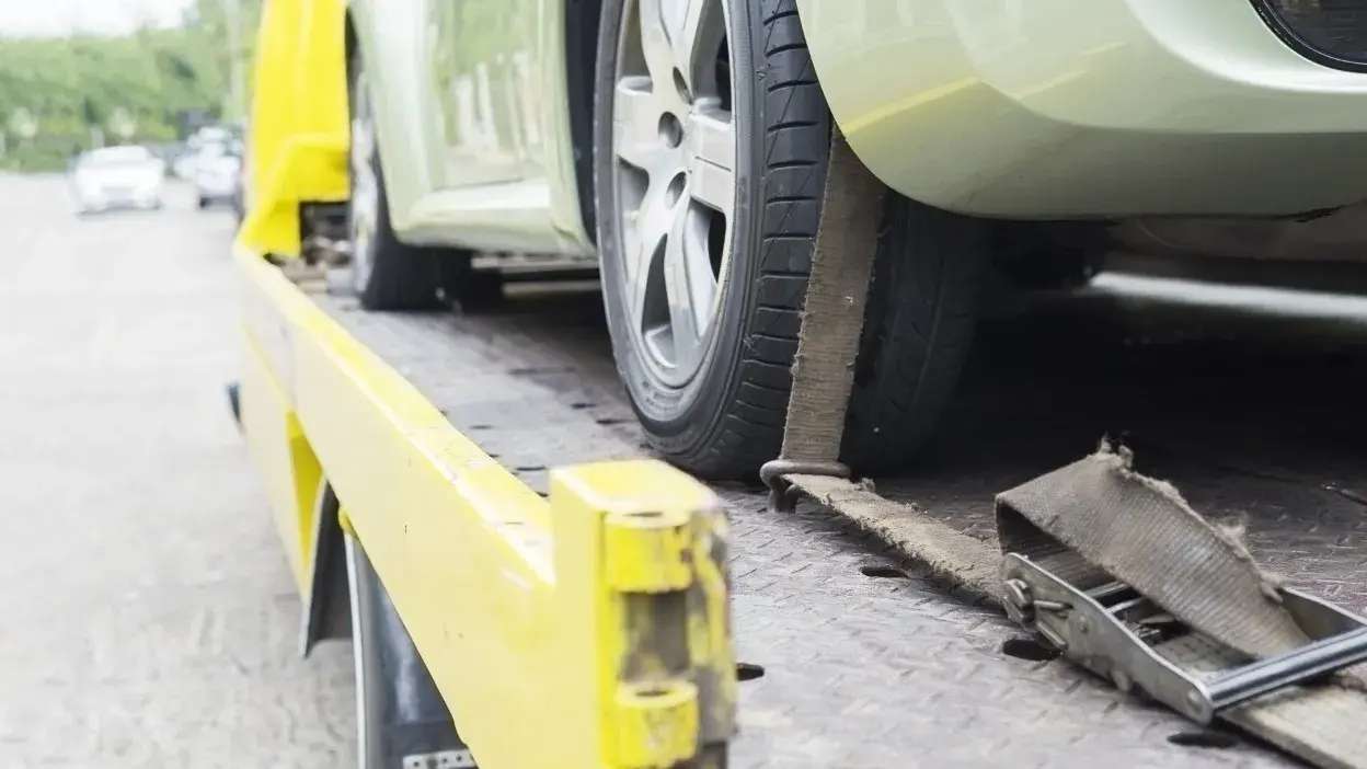 Carro preso com cinta numa plataforma de reboque amarela na berma da estrada
