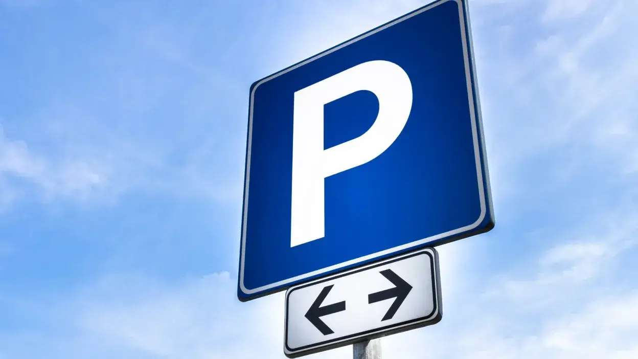 Sinal azul com a letra P branca indicando estacionamento, com placa inferior de setas para os dois lados, céu azul ao fundo