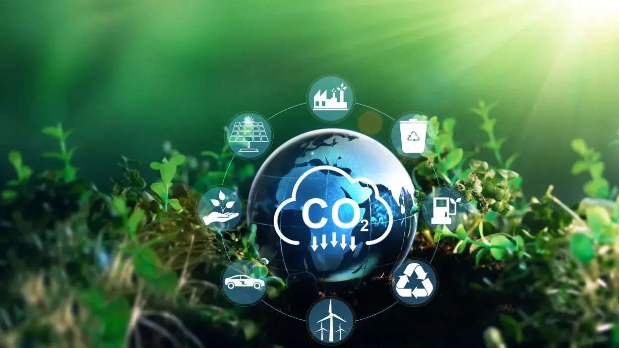 Globo terrestre rodeado por ícones de energia renovável, reciclagem e sustentabilidade ambiental sobre plantas verdes.