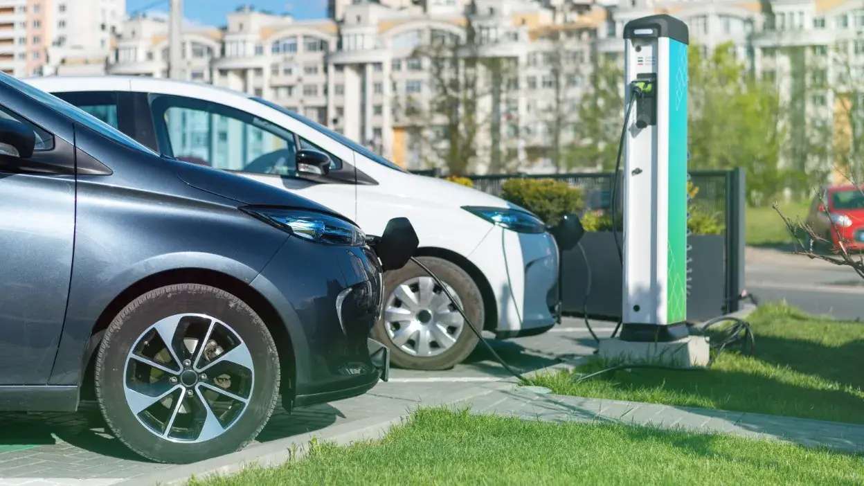Dois carros elétricos a carregar numa estação de carregamento exterior numa área urbana.