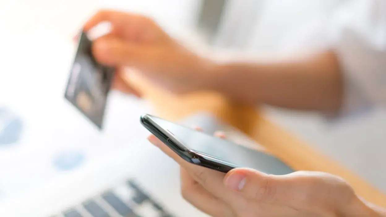 Pessoa a segurar telemóvel e cartão de crédito para pagamento online