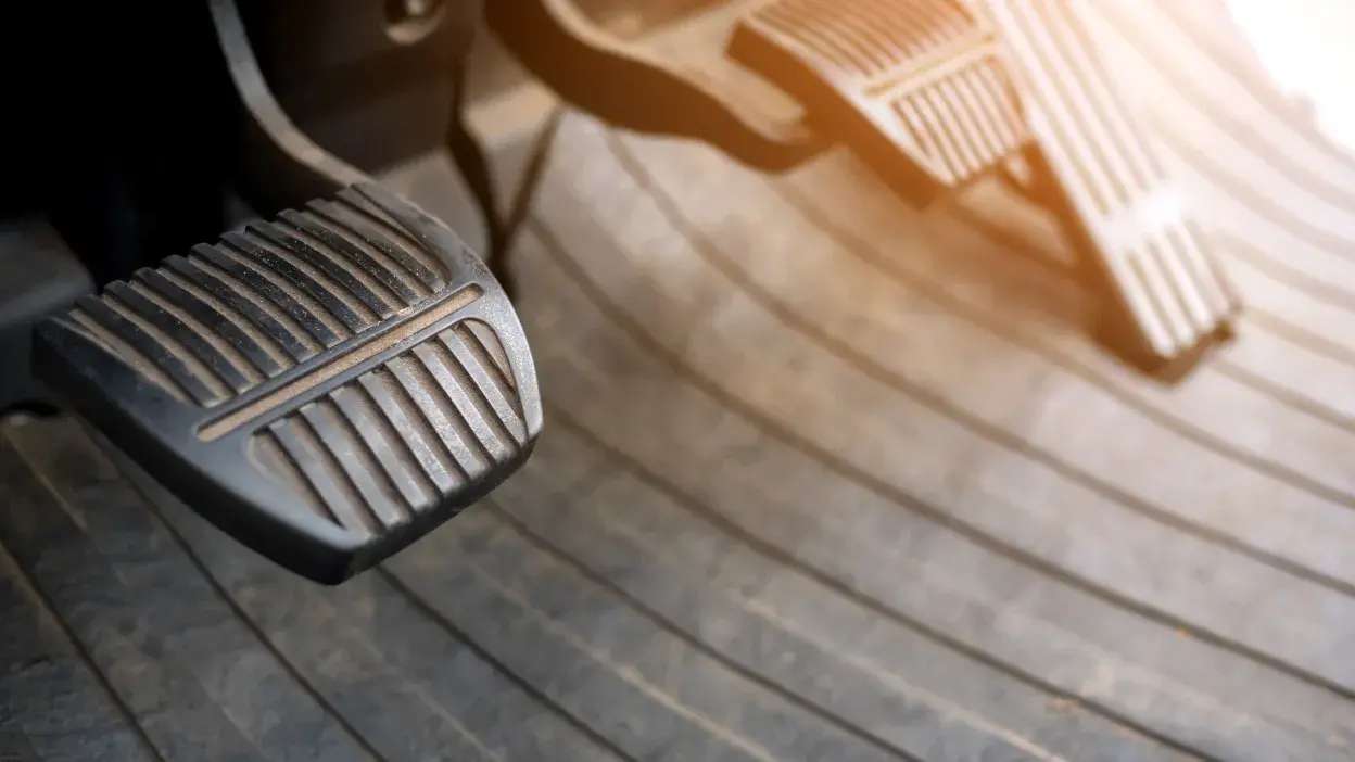 Pedais de embraiagem e travão de um carro com luz solar a incidir.