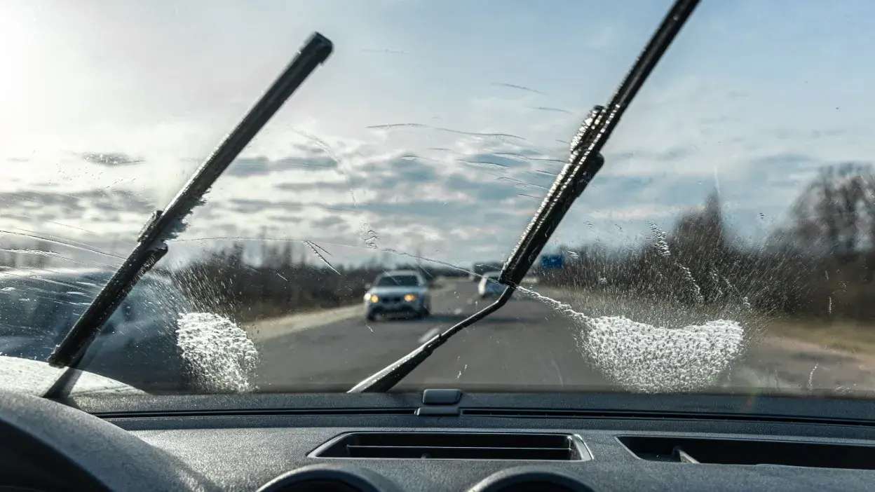 Vista interior de carro com limpa para-brisas a limpar parcialmente o vidro dianteiro sujo.