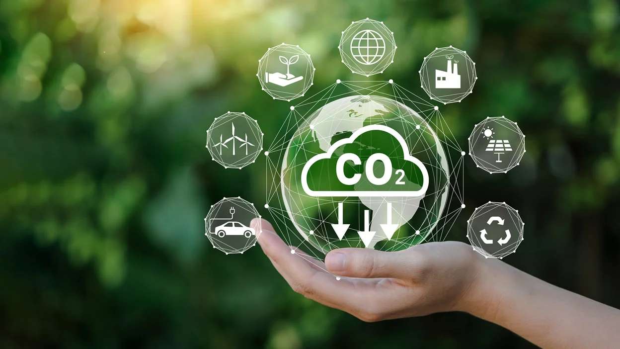 Mão segurando globo terrestre com ícones de sustentabilidade e redução de emissões de CO2.