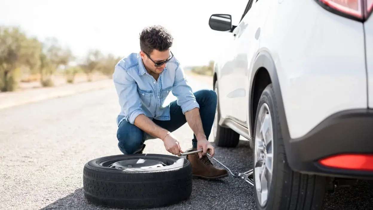 Homem a usar macaco para levantar carro e trocar pneu na berma da estrada
