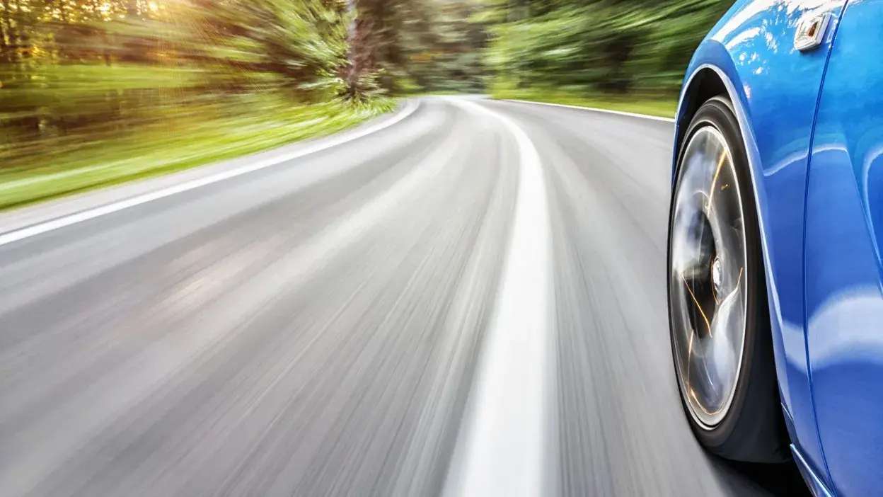 Roda de carro azul em movimento rápido numa estrada curva rodeada de árvores verdes