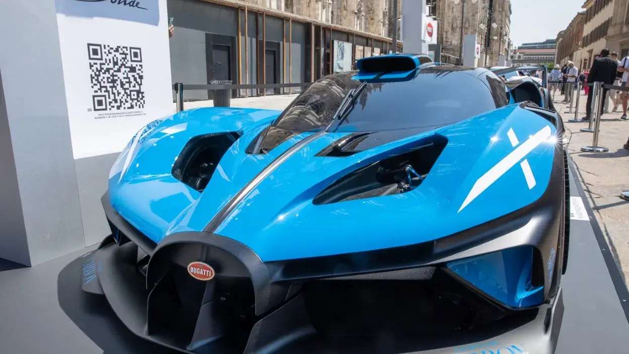 Carro desportivo Bugatti azul exposto numa rua com pessoas ao fundo.