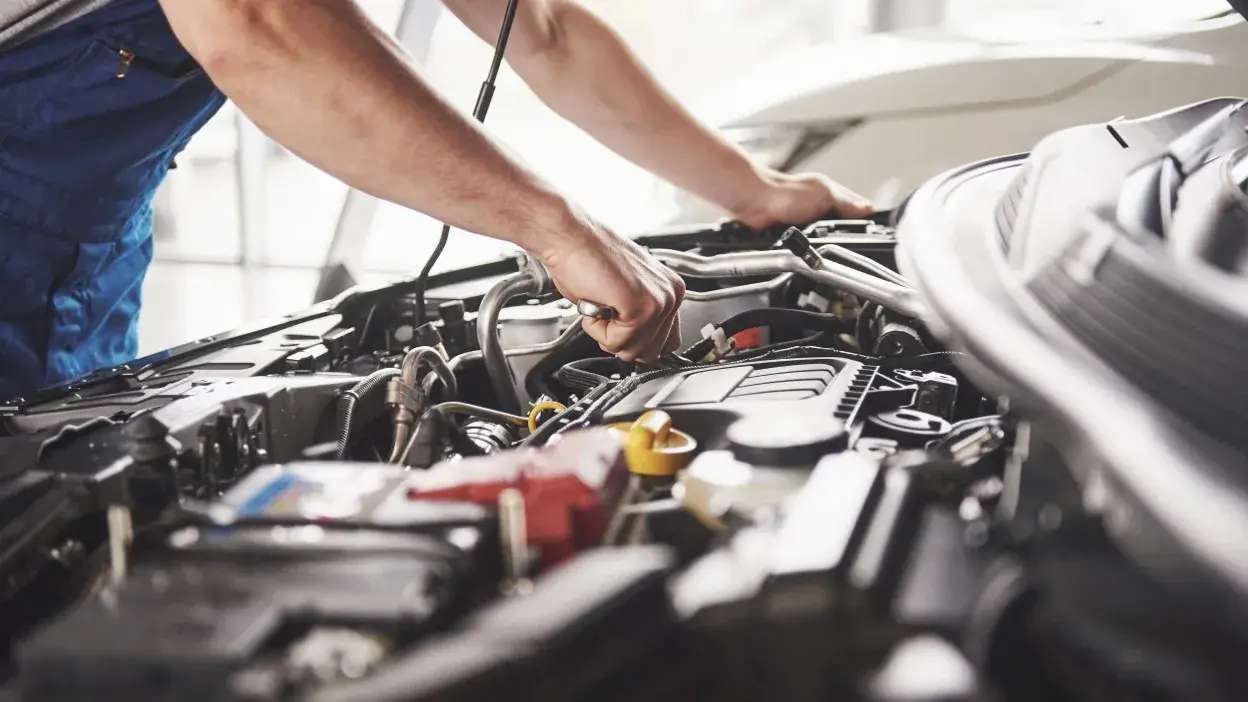 Mãos de mecânico a trabalhar no motor de um carro com ferramenta.