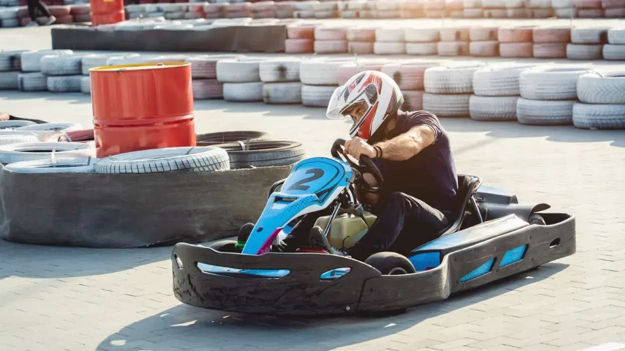 Homem com capacete a conduzir kart num circuito com pneus de proteção.