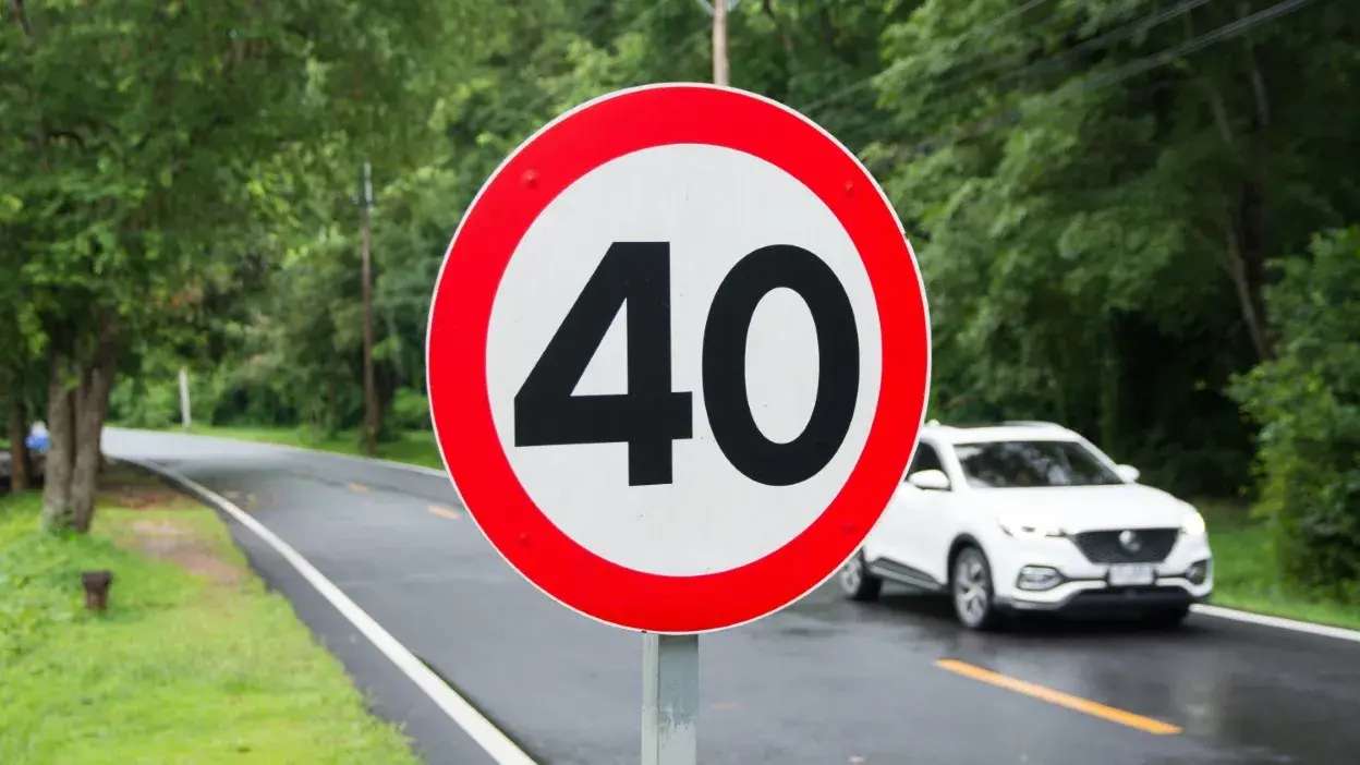 Sinal de trânsito a indicar limite de velocidade de 40 km/h numa estrada com carro branco ao fundo