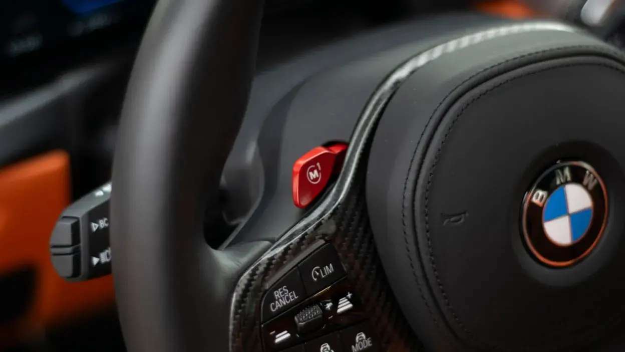 Volante de BMW com botões de controlo e detalhe em carbono e vermelho.