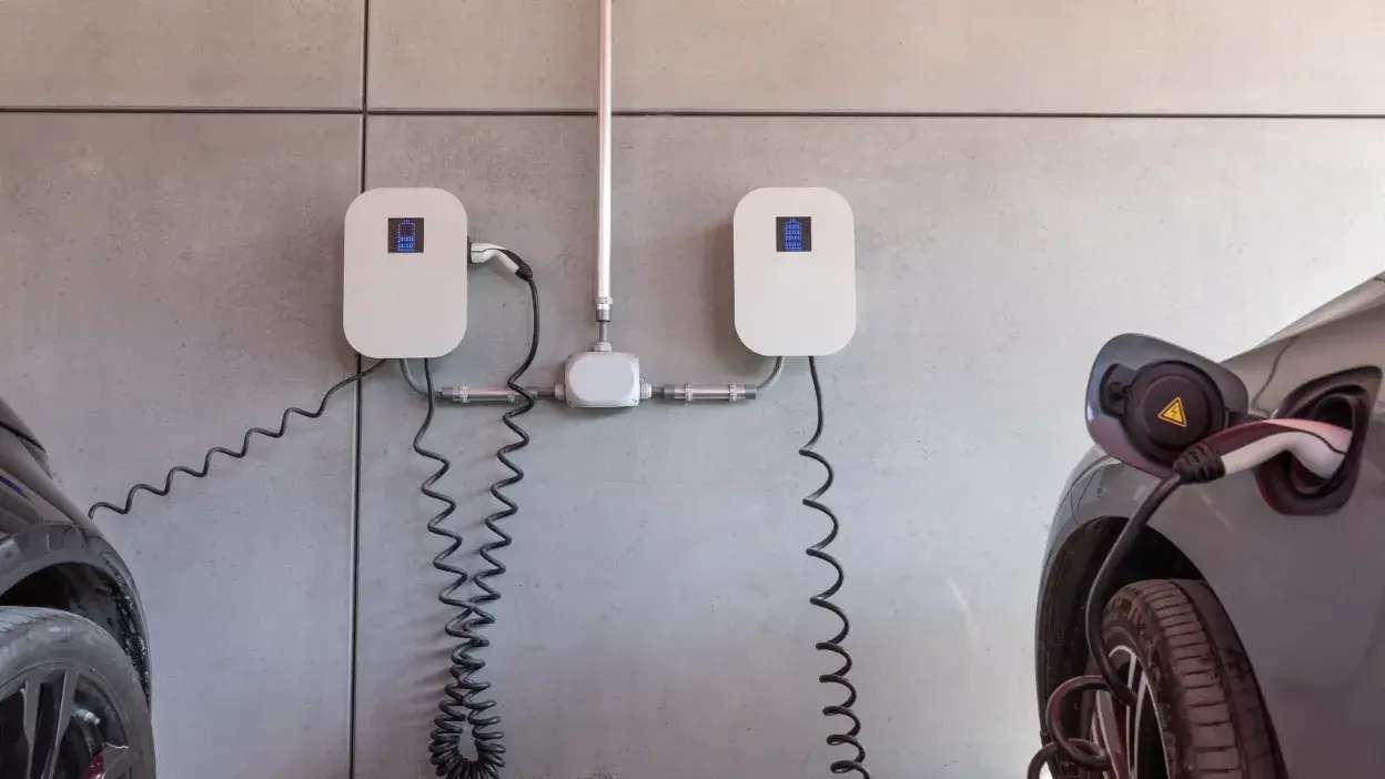 Dois carros elétricos a ser carregados em estações de carregamento montadas numa parede cinzenta.
