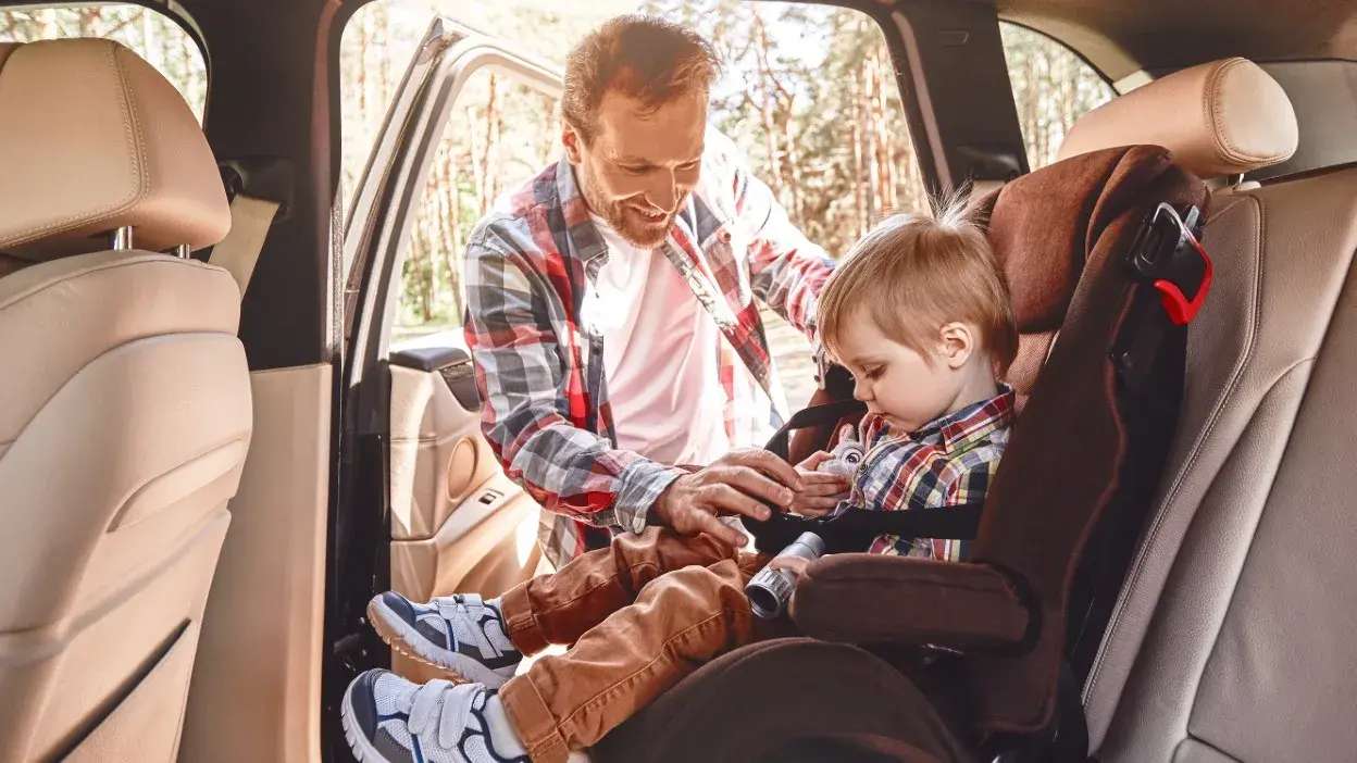 Pai a prender criança no cadeirão auto dentro do carro.