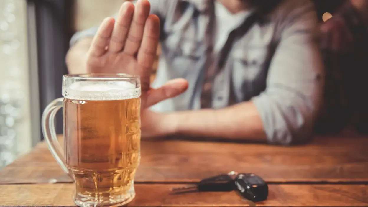 Pessoa a recusar uma caneca de cerveja com chaves de carro na mesa.