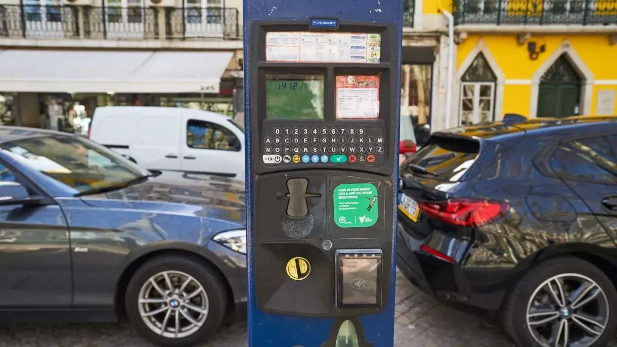 Parquímetro azul da EMEL para pagamento de estacionamento em Lisboa, com teclado e leitor de cartões, rodeado por carros estacionados.