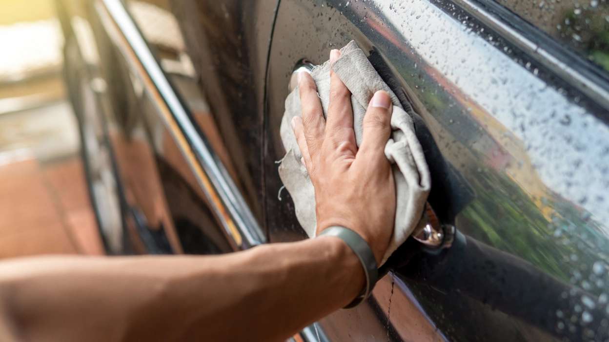 mão de um homem a limpar a parte exterior da porta do carro com um pano
